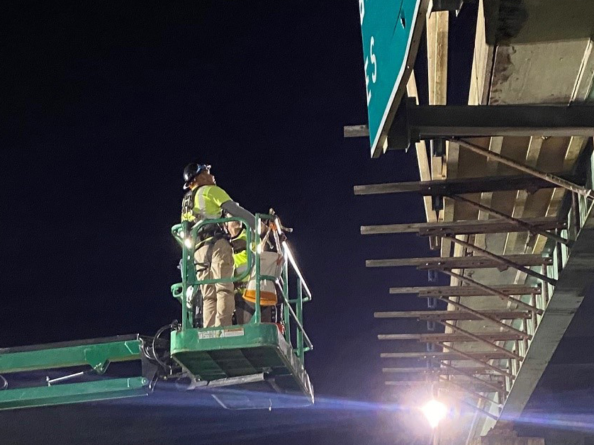 Workers access the bridge from a cherrypicker at night.